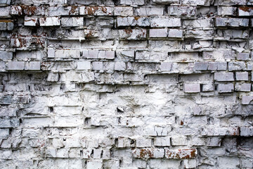 old, beaten, white brick wall with many rockfalls and cracks