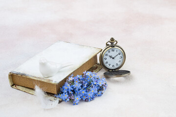 forget me nots in a book, pocket watches, feathers and a porcelain figurine of a bird