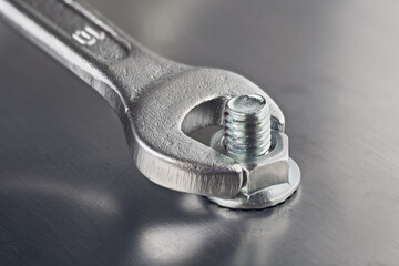 Wrench tightens  bolt in steel billet. Spanner, bolt, screw and nuts. - obrazy, fototapety, plakaty