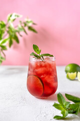 Berry cocktail with mint and lime garnish on pink background