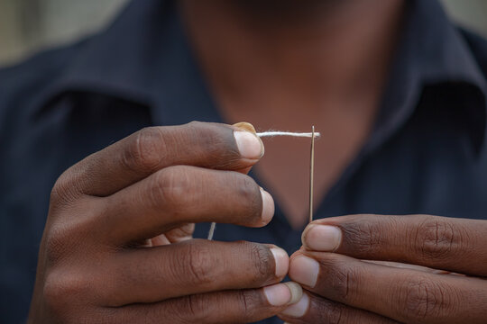 a poor man hand threading needle and trying to put the thread inside the needle