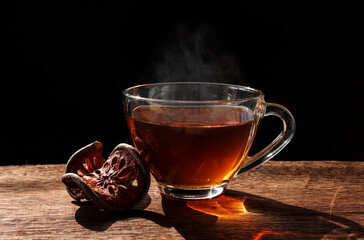 The Bael fruit juice in a glass and dried Bael fruit placed on the wooden floor with black background.Drinking Bael fruit juice in the morning will help the body to refresh.