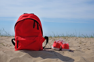 red backpack and shoes on a beach background travel concept