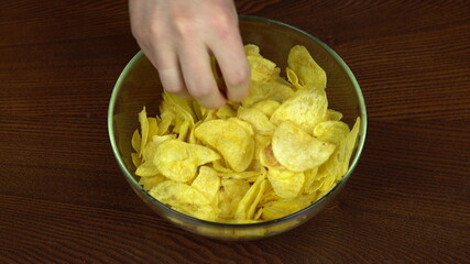 The hands of people actively taking chips from a large dish. The company of friends eats potato chips. Hands close up. Hungry people