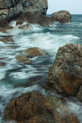 Sea summer landscape with blurred waves, rocks on the beach, large rocks on the shore close-up, background of other rocks sticking out of the water.