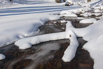Small flowing river landscape in winter, in the river lie the letter x two trees covered with snow.