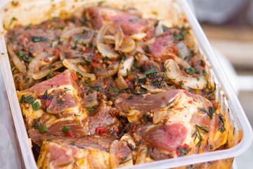 Raw marinaded juicy pork meat in plastic container. Fresh food prepared for barbeque. Summer cooking outdoors