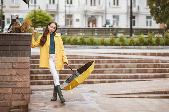 A young pretty teenage girl walks around the city in rainy weather. The girl is dressed in colored clothes and rubber boots