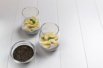 Chia pudding with mint leaves in glass cups with grains in a bowl on a white background. Copy...