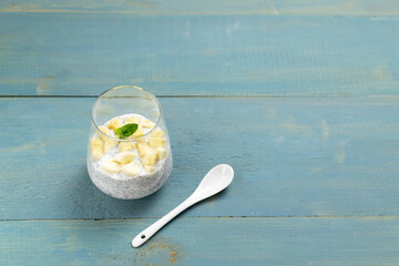 Chia pudding with a sprig of mint in a glass cup with a teaspoon on a blue wooden background. Copy space. A healthy breakfast consists of yogurt and grains. Selective focus
