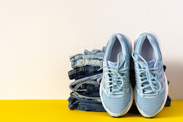 A stack of different jeans trousers and blue sneakers close up on yellow and white background, casual clothes , sports style