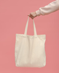 A woman's hand holds a trendy bag on a pink background. The concept of zero waste. Reusable light cotton shopper bag for going to the supermarket instead of plastic bags.