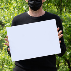 Man in Medical Black Mask holding a White Banner with Space for Text isolated on black