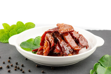 Deep fried sun dried pork in white dish with kaffir lime leaves and pepper seeds on slate plate