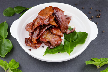 Deep fried sun dried pork in white dish with kaffir lime leaves and pepper seeds on slate plate