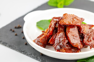 Deep fried sun dried pork in white dish with kaffir lime leaves and pepper seeds on slate plate