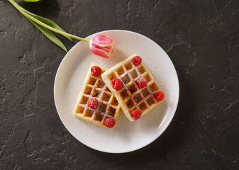 Viennese homemade waffles with red raspberries lie on a plate on a table with a pink flower nearby