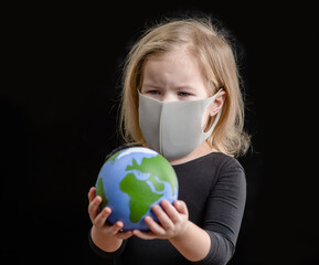 Little girl wearing protective mask holds planet Earth. The concept of a global warming or coronavirus pandemic