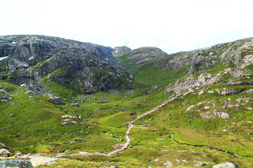 Fototapeta na wymiar Panoramatic view of a hiking trail with a pathway, rocks and stream in a green valley which is a part of the famous Kjerag trail in Norway.