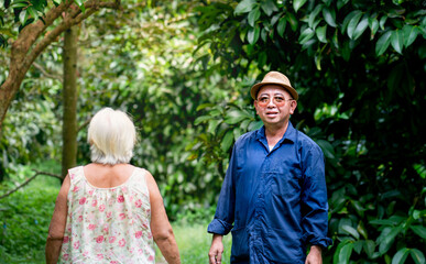 Happy Thai gardener man and grandmother walking at his organic garden. Sufficiency economy.Proud with success gardener man with organic orchards such as durian, rambutan, longkong, pepper, mangosteen.