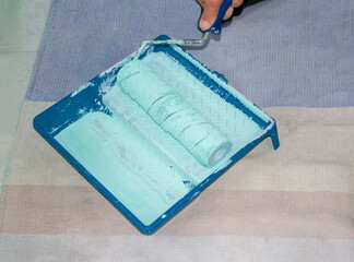 Plastic tray with turquoise paint and soft dirty paint roll brush in mint paint. Tools for the painter and redecoration on the carpet, on the floor. Interior renovation.