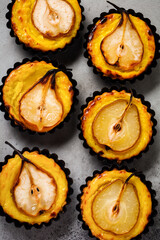 Pears and custard mini tarts on a dark gray concrete old table background. Top view.