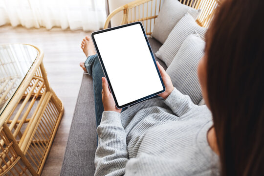 Top view mockup image of a woman holding black tablet pc with blank desktop white screen while lying on a sofa at home