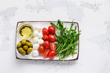 Mozzarella, cherry tomatoes and arugula served in white ceramic rectangular plates with olive oil over grey texture background. Flat lay