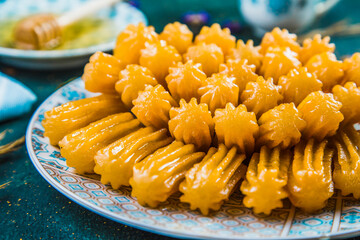 Turkish syrupy dessert tulumba arranged in plate. Fried pastry coated in sugar syrup on table with honey dipper and plate.