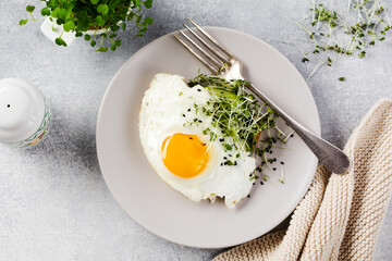 Traditional English breakfast with fried eggs with arugula microgreen in gray ceramic plate on gray concrete old background. Top view.