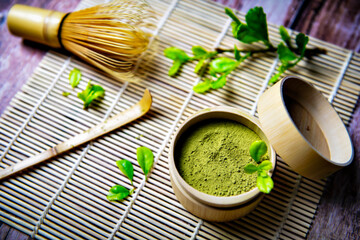 Green Tea Matcha Powder in the Bamboo Cup with Wooden Chasen in Matcha Tea Bowl and Wooden Spoon and on Wooden Background