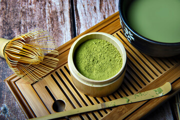 Green Tea Matcha Powder in the Bamboo Cup with Wooden Chasen in Matcha Tea Bowl and Wooden Spoon and on Wooden Background