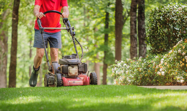 Mowing grass with a gas powered lawn mower. Male landscaper cutting residential backyard with walk behind mower. 