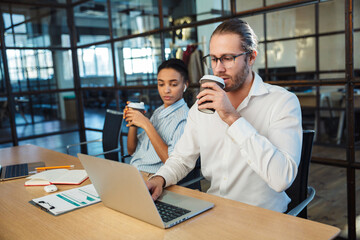 Photo of serious colleagues working with laptops and drinking coffee