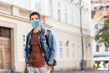 Fototapeta premium Handsome man with illustrated face in medical mask and hands in pockets on street