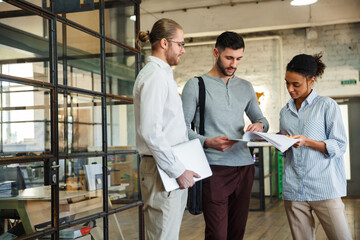 Photo of multinational focused colleagues talking and reading documents
