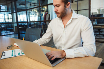 Fototapeta premium Photo of handsome focused man making notes and working with laptop