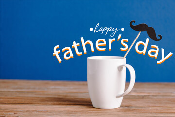 white cup and black decorative paper fake mustache on wooden surface isolated on blue, happy fathers day illustration