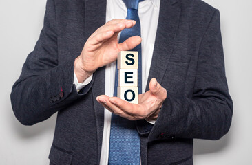 Text word seo on a wooden cube blocks in hand of a businessman in suit. SEO concept