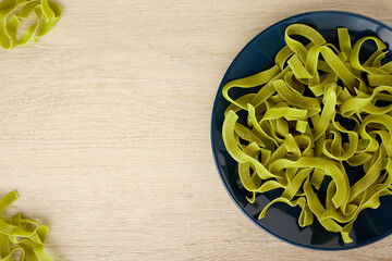 Raw green pasta with spinach on a dark blue plate, top view, copy space