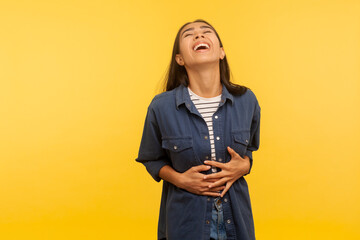 What a funny joke! Portrait of amused carefree girl in denim shirt cracking up with hilarious...