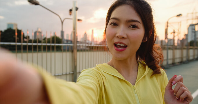 Attractive young Asia athlete influencer lady recording video vlog live streaming on phone upload in social media while exercises in urban city. Sportwoman wearing sports clothes on street in morning.
