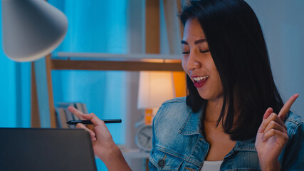 Freelance smart business women listening music after use laptop work hard in workplace in living room at home at night. Happy young Asian girl sitting on desk work overtime, dance enjoy relax time.