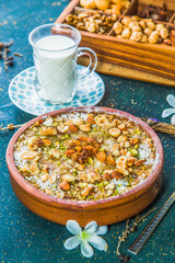 Um Ali dessert with chopped nuts and raisins. Egyptian bread pudding on table with cup of milk and wooden box with nuts.