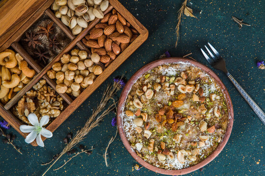 Wooden box full with nuts next to Egyptian bread pudding. Oriental dessert Om Ali on table next to opened wooden box with hazelnuts, star anise, cashew, pistachio, walnuts and almonds.