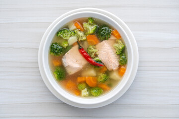 Fresh salmon fish soup with carrots, potatoes, red peppers, green broccoli and onions in a white plate, close up. Tasty dinner consists of a fish soup with salmon