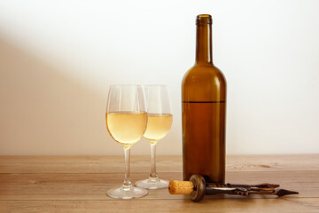 Glass bottle of wine, two filled glasses and a corkscrew on a wooden background.
