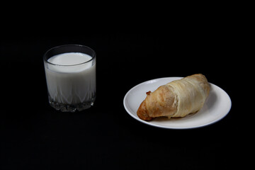 croissant on a plate and a glass of milk on black background