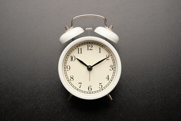 White vintage alarm clocks show 10:10 isolated on black table background.