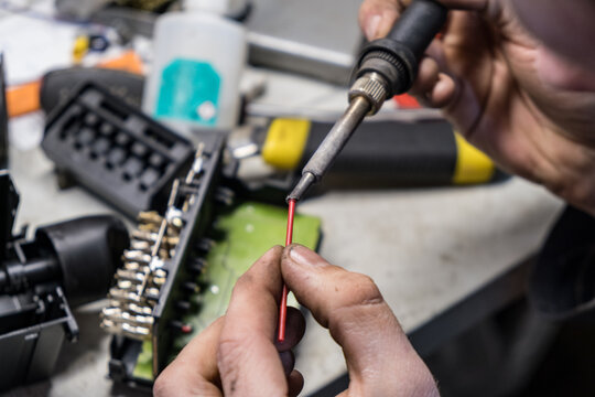 Close up view of male hands soldering piece of wiring. Electric car light controller repair.